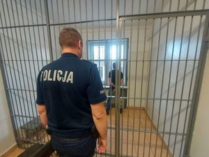Policjant stojący przed kratą, w tle mężczyzna
