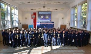 W pomieszczeniu grupa umundurowanych policjantów w tle godło i flaga państwowa