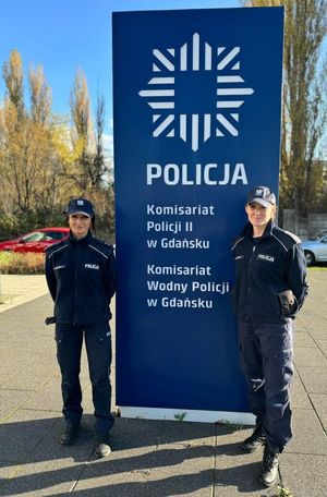 Zdjęcie dwóch policjantek obok baneru komisariatu Policji