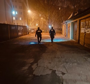 Dwóch policjantów idących w scenerii nocnej pomiędzy ciągami garaży