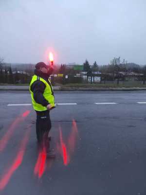 Policjant w kamizelce odblaskowej zatrzymujący latarką pojazd na jezdni