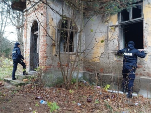 Dwóch policjantów lustrujących z zewnątrz murowany pustostan bez okien