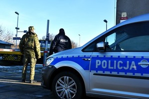 Policjant ze strażnikiem granicznym stoją przy radiowozie policyjnym