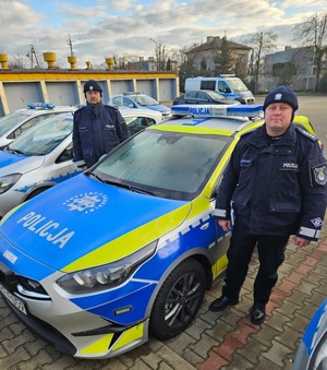 Dwaj policjanci obok radiowozu na placu