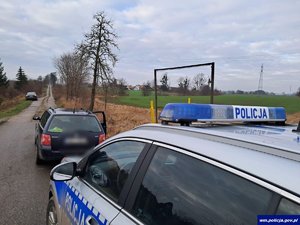 Na polnej drodze radiowóz, a przed nim czarny samochód kombi