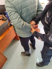 Policjant zakłada kajdanki na ręce trzymane z tyłu zatrzymanemu mężczyźnie
