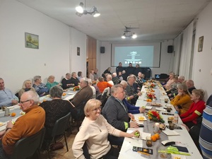 Seniorzy przy stolach w sali konferencyjnej podczas prelekcji prowadzonej przez policjantów