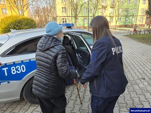 Policjantka przytrzymująca staruszkę przy otwartych drzwiach radiowozu