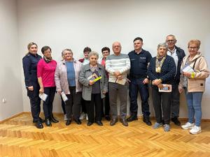Grupa seniorów z ulotkami w rękach oraz dwójka policjantów pozująca w pomieszczeniu do zdjęcia