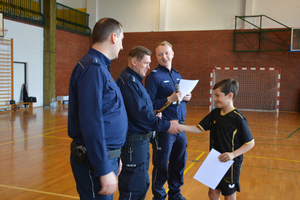 Trzech policjantów wręczających na sali gimnastycznej chłopcu dyplom