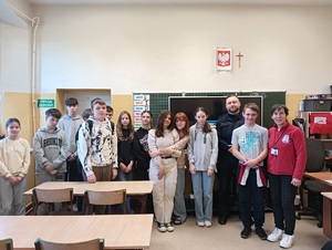 Młodzież w sali szkolnej pozująca do zdjęcia wraz z policjantem