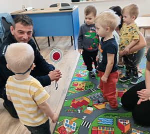 Policjant kucający do grupki dzieci w sali przedszkolnej