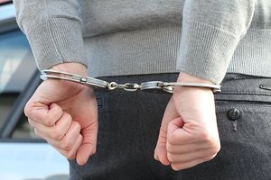 Plecy mężczyzny w szarym swetrze ze skutymi kajdankami rękami