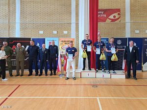 Zdjęcie sali sportowej z podium i zawodnikami oraz stającymi z boku policjantami i żołnierzami