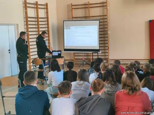 Dwaj policjanci prowadzący prelekcje dla młodzieży zgromadzonej w sali gimnastycznej