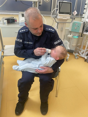 Policjant karmiący na kolanach buteleczką niemowlaka