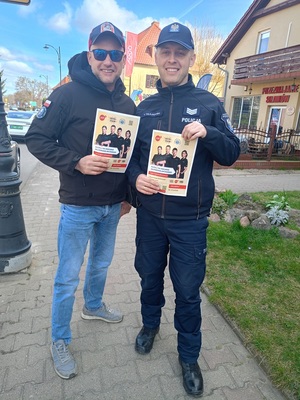 Uśmiechnięty policjant oraz młody mężczyzna z plakatami kampanii #SuperDzielnicowy