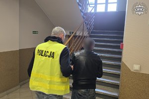 Policjant w kamizelce odblaskowej prowadzący po schodach mężczyznę ze skutymi rękami