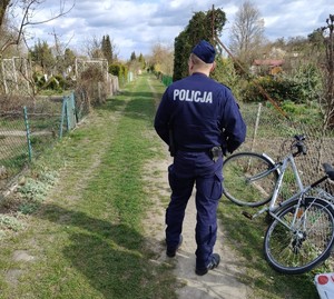 Policjant obok roweru na ścieżce w ogródkach działkowych