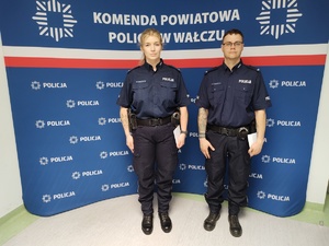 Dwójka policjantów pozująca na tle ścianki KPP w Wałczu