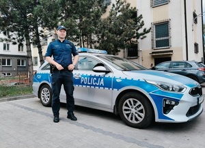 Policjant w otwartej przestrzeni na tle radiowozu