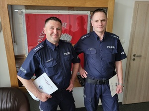 Dwaj policjanci na tle gabloty ze sztandarem jednostki