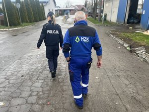 Widziani od tylu idący ulica: policjantka i mężczyzna w niebieskim kombinezonie roboczym
