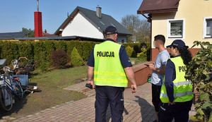 Dwójka policjantów i mężczyzna przed posesją z domem jednorodzinnym