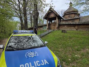 Zabytkowy, drewniany budynek sakralny na tle zieleni, na pierwszym planie radiowóz