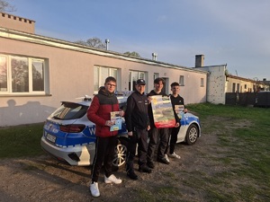 Policjant oraz trzech młodych chłopców na tle radiowozu