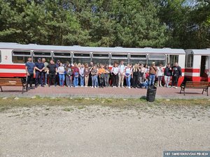 Grupa młodzieży oraz dwóch policjantów pozujących do zdjęcia na tle wagonu kolejowego w kolorze kremowo-czerwonym