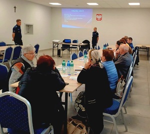 Dwójka policjantów prowadząca w sali konferencyjnej prelekcje do zgromadzonych seniorów.