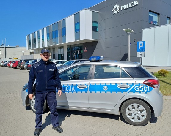 Policjant na tle radiowozu i budynku komendy