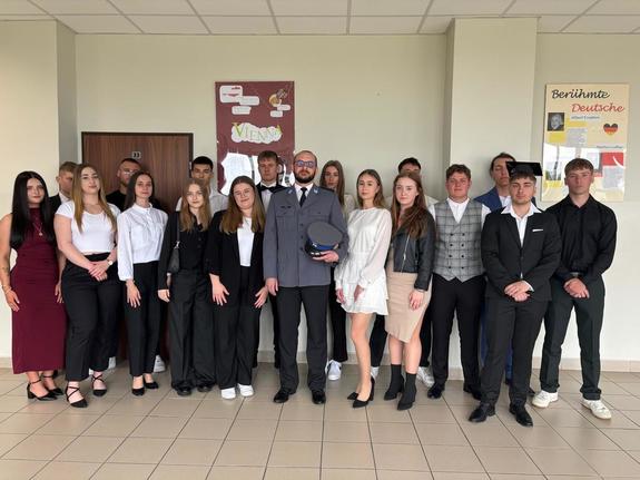 Pozująca do zdjęcia w sali szkolnej grupa młodzieży oraz policjant
