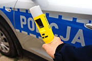 Trzymany w ręce policjanta alkotest na tle radiowozu