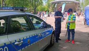 Policjant oraz młody chłopak obok radiowozu na tle pikniku