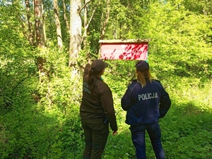 Na tle zieleni i tablicy rezerwat przyrody strażniczka leśna i policjantka