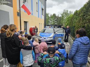 Grupa dzieci na placu przed szkołą oraz radiowóz i policjant