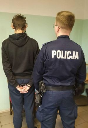 Widziani od tylu w areszcie mężczyzna ze skutymi rękami oraz policjant