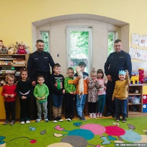 Wewnątrz sali przedszkolnej grupa przedszkolaków oraz dwóch policjantów pozująca do zdjęcia
