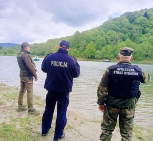 Widziani od tyłu policjant oraz strażnik leśny na brzegu akwenu