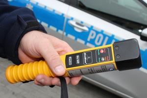 Ręka policjanta trzymająca alkotest na tle radiowozu