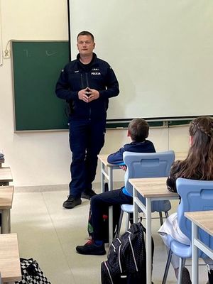 Policjant prowadzący w sali szkolnej pogadankę dla dzieci
