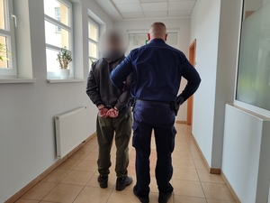widziani od tyłu policjant prowadzący korytarzem skutego kajdankami mężczyznę