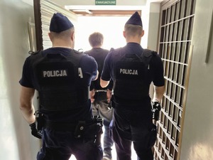 Dwaj policjanci w korytarzu prowadzący skutego kajdankami mężczyznę