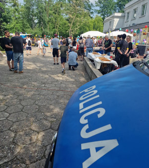 Piknik rodzinny na placu, w tle zieleń, na pierwszym planie maska radiowozu