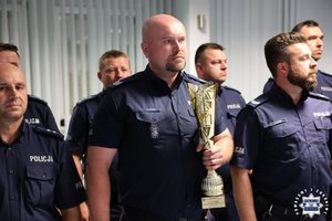 Policjanci stojący w szeregu, wśród nich na pierwszym planie policjant trzymający w ręce puchar