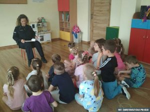 Policjantka czytająca  książkę dzieciom siedzącym na podłodze sali przedszkolnej