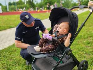 Policjant kucający przy dziecku w spacerówce