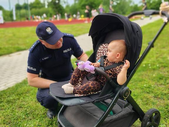 Policjant kucający przy dziecku w spacerówce